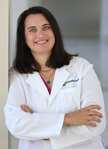 A smiling doctor in a white coat stands confidently with her arms crossed.