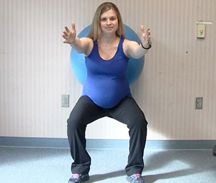 A pregnant woman is performing a wall squat exercise using an exercise ball.