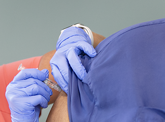 person wearing blue gloves is giving an injection to someone.