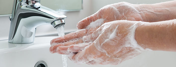A person washing their soapy hands under running water in a sink.