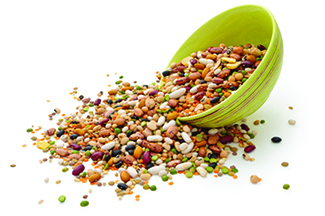 The image shows a green bowl tipped over, spilling a colorful mix of dried beans and legumes.