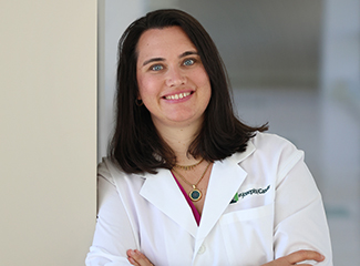 A smiling female doctor in a white coat stands confidently with her arms crossed.