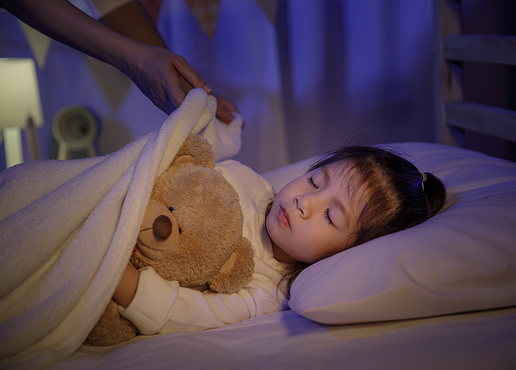 A small kid with a teddy is being tucked into bed.