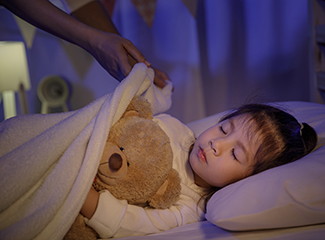 A small child with a teddy being tucked into bed to sleep.