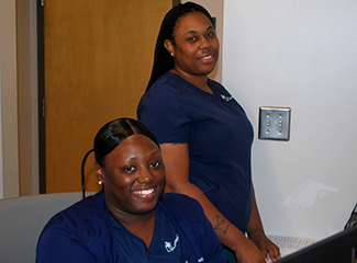 Two women in scrubs smiling and standing together.