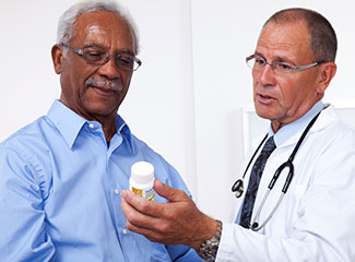 A doctor is showing a medication bottle to an older man during a consultation.