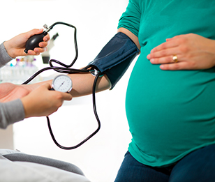 A healthcare provider measures the blood pressure of a pregnant woman in a clinic.