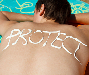 The word "PROTECT" is written with sunscreen on a person's back as they lie in the sun.