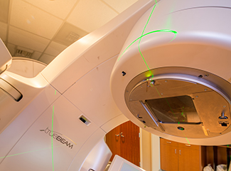 The image shows a TrueBeam radiotherapy machine used for stereotactic body radiation therapy (SBRT), with green laser guides visible.