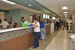 A busy hospital hallway featuring individuals gathered around the reception counter, engaged in conversation and assistance.