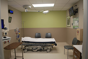 Interior of a hospital room with a bed, a chair, and a television.