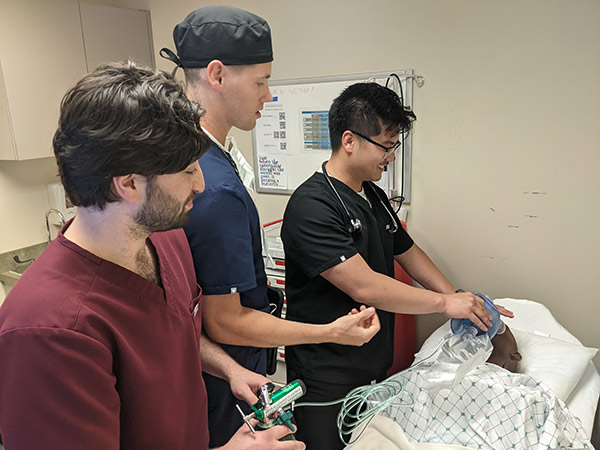 Three healthcare professionals in scrubs stand around a patient, engaged in a discussion about the patient's care and treatment.